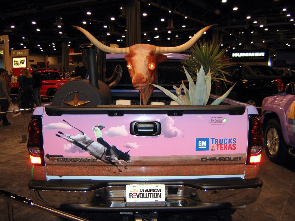 Rear of a light purple Chevrolet Silverado with a longhorn skull, plants, and a rodeo graphic on the tailgate. GM Trucks for Texas logo visible