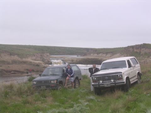 1986 Ford Bronco - Two SUVs are parked on a grassy hill overlooking a waterfall.