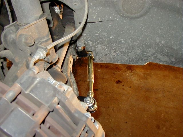 Gold zinc adjustable sway bar end link installed on rusty rear suspension, underbody view