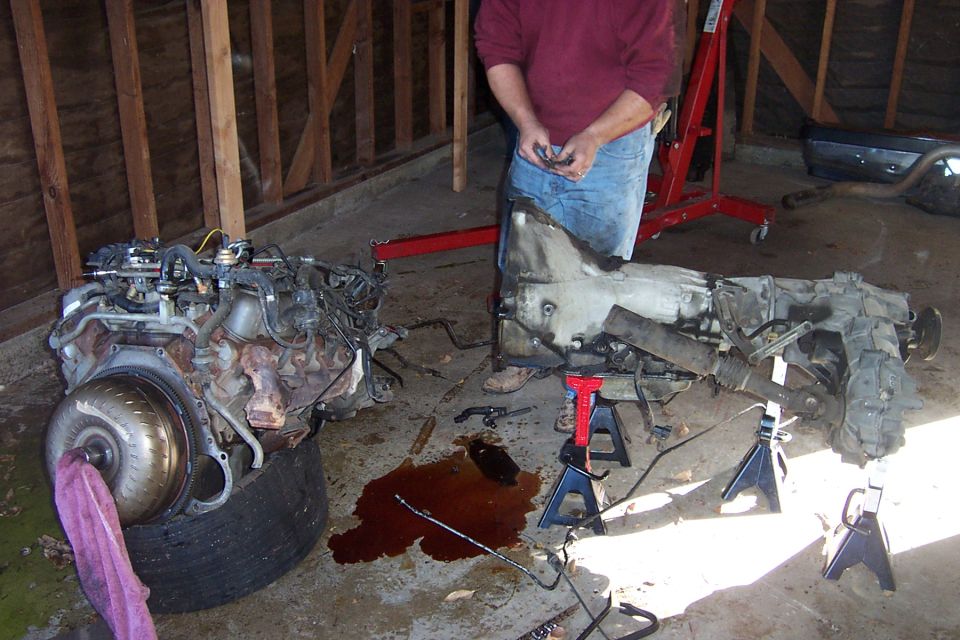 Removed V8 engine on a tire beside a transmission and transfer case on jack stands in a garage