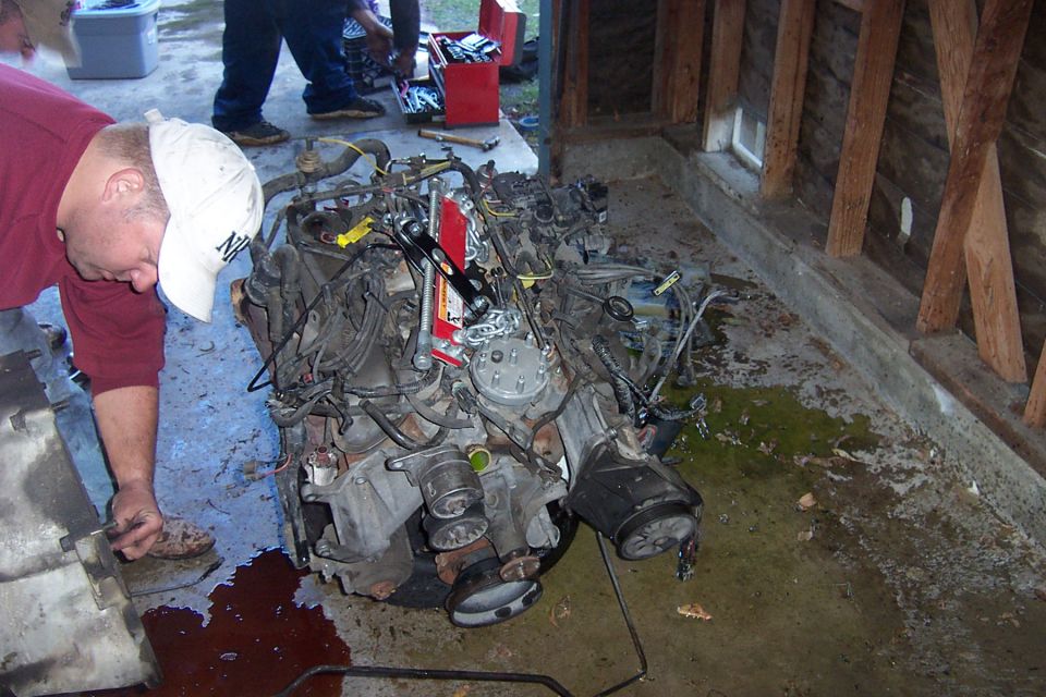 Man in red shirt working on a pulled engine sitting on a shop floor with oil spill