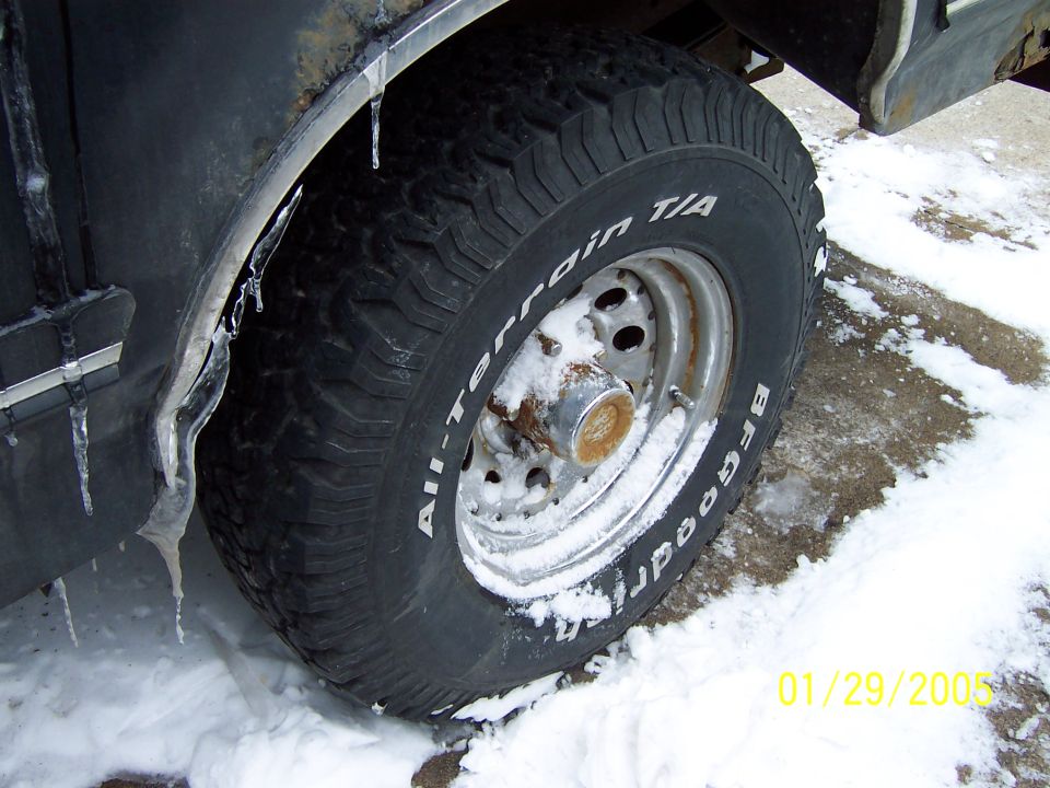 Black vehicle fender with icicles, BFGoodrich All-Terrain T/A tire on a silver rim, snow on ground