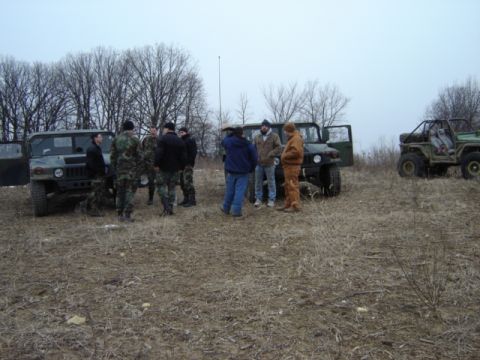 1992 Ford Bronco - Several individuals gather near military vehicles in an outdoor, barren landscape.