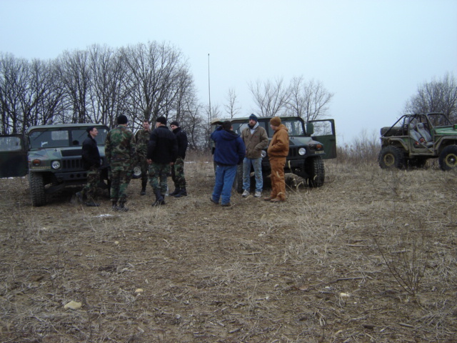 Group of people standing around two military-style vehicles in a field