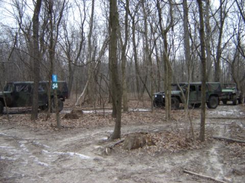 1992 Ford Bronco - Two military vehicles navigate a wooded trail, with one towing a trailer behind it.