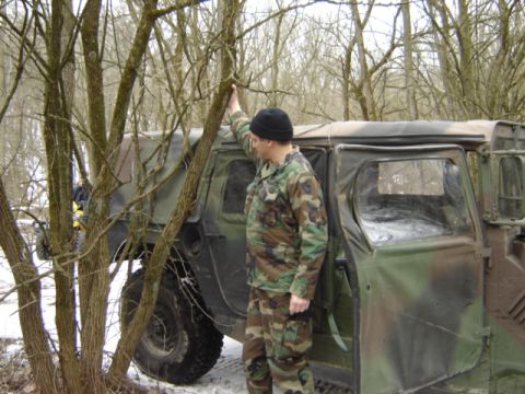1992 Ford Bronco - A man in camouflage stands by a military vehicle in a snowy, wooded environment.