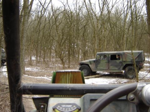 1992 Ford Bronco - A military vehicle navigates a snowy, wooded trail, with another vehicle's interior visible in the foreground.