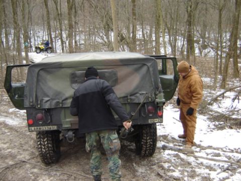 1992 Ford Bronco - A Humvee is seen from the rear in a snowy, wooded environment with two individuals attending to it and an ATV visible on a hill.