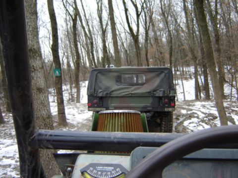 1992 Ford Bronco - A camouflaged military vehicle is seen from another vehicle in a wooded area with snow on the ground.