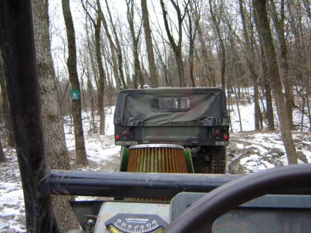 View from inside a vehicle looking at the rear of a camouflaged military truck in a snowy forest