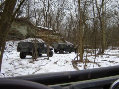 1992 Ford Bronco - Two military trucks are parked in a snowy, wooded environment with a rocky cliff in the background.