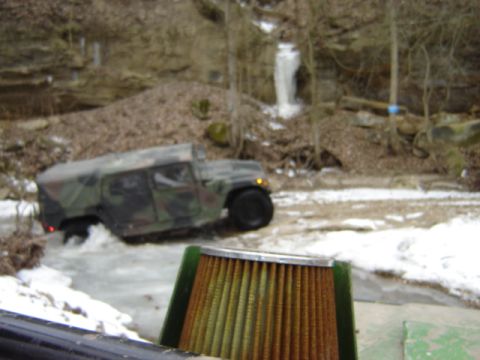 1992 Ford Bronco - A camouflaged Humvee navigates through a shallow, icy stream with a frozen waterfall in the background.