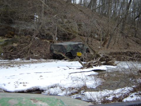 1992 Ford Bronco - Military vehicle stuck in snow and ice next to a wooded hillside.