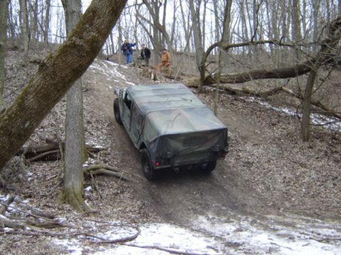 1992 Ford Bronco - A military vehicle navigates a wooded trail with several people observing from a higher elevation.