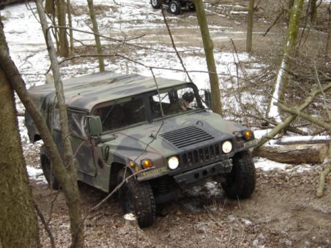 1992 Ford Bronco - A camouflaged Humvee navigates a wooded trail with snow on the ground.