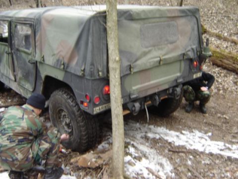 1992 Ford Bronco - A camouflage military vehicle is seen from the rear with two individuals in camouflage gear in the vicinity.