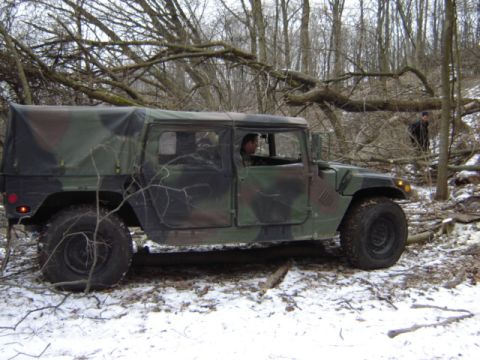 1992 Ford Bronco - A camouflaged Humvee navigates a snowy, wooded terrain with fallen branches obstructing the path.