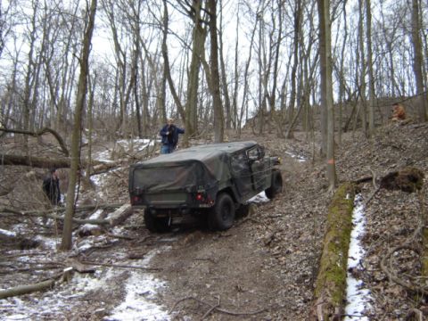1992 Ford Bronco - Military vehicle navigates a wooded trail with fallen trees and snow patches.