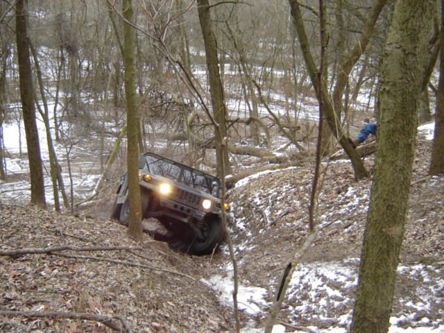 Hummer H1 driving down a wooded, snowy hill