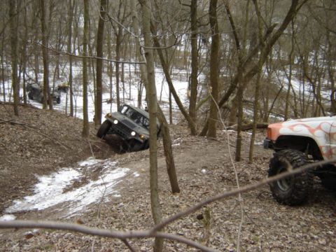 1992 Ford Bronco - A gray Humvee maneuvers through a wooded area with snow on the ground, while another off-road vehicle is partially visible in the foregroun…