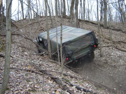 1992 Ford Bronco - A military vehicle navigates a wooded trail, its camouflage top blending with the forest surroundings.