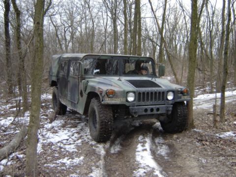 1992 Ford Bronco - A camouflaged Humvee navigates a wooded trail with patches of snow on the ground.