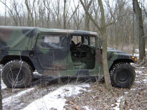 1992 Ford Bronco - A camouflaged military vehicle is parked off-road in a wooded area during winter.