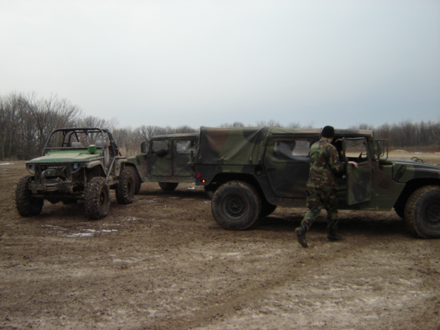 Two military Humvees and a green off-road vehicle on a dirt track