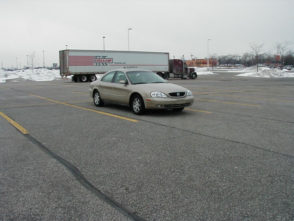 Gold Mercury sedan in a snowy empty parking lot with a Kreilkamp semi trailer behind