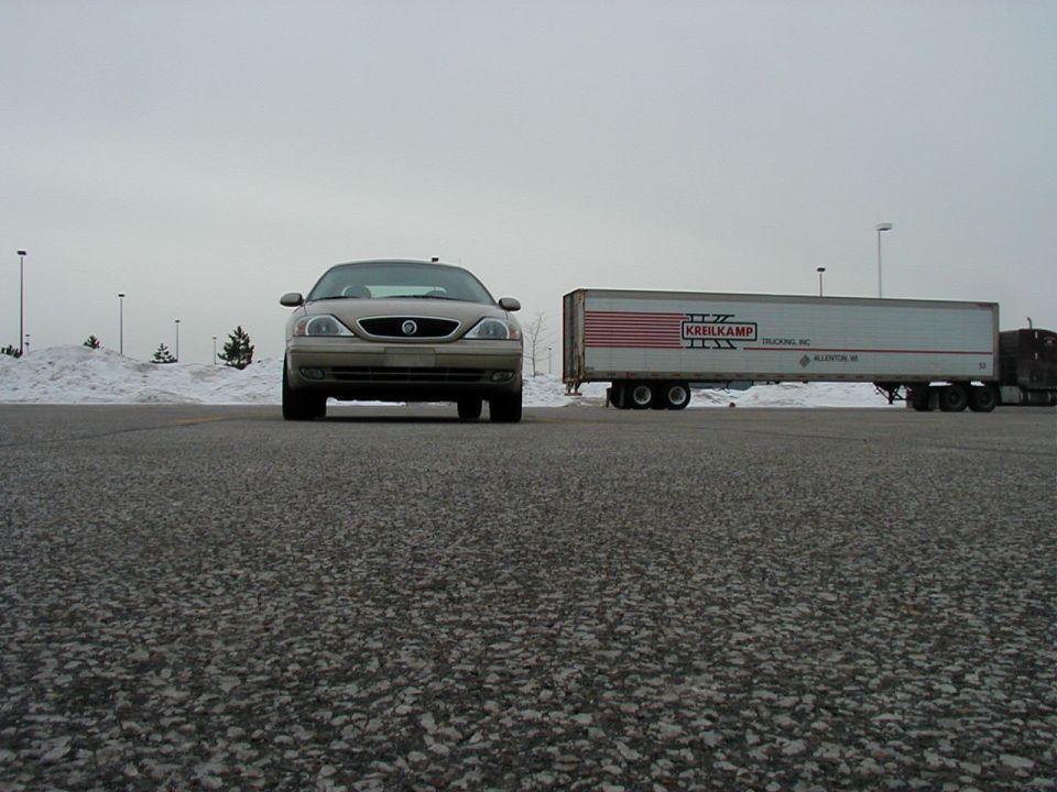 Tan Mercury Sable parked in front of a white semi-trailer truck