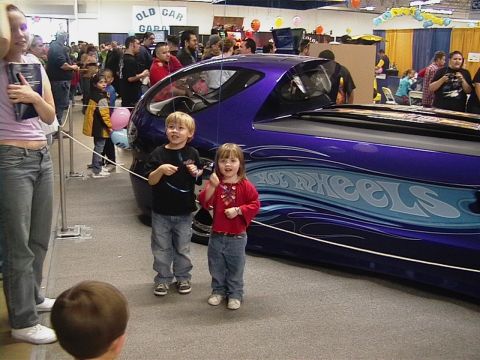 1999 Ford Taurus - Children stand next to a customized purple vehicle with 'Hot Wheels' graphics at an indoor event.