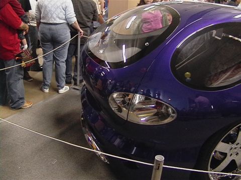 1999 Ford Taurus - A unique custom car with an unusual design is displayed indoors, drawing attention from onlookers.