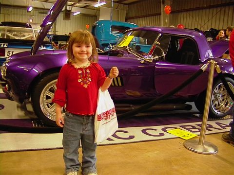 1999 Ford Taurus - A young girl poses in front of a purple sports car at a car show.