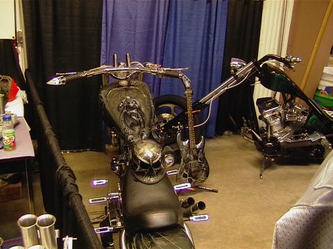 1999 Ford Taurus - A custom motorcycle with intricate artwork and a skull helmet is displayed alongside another motorcycle, with an electric guitar as a prop.