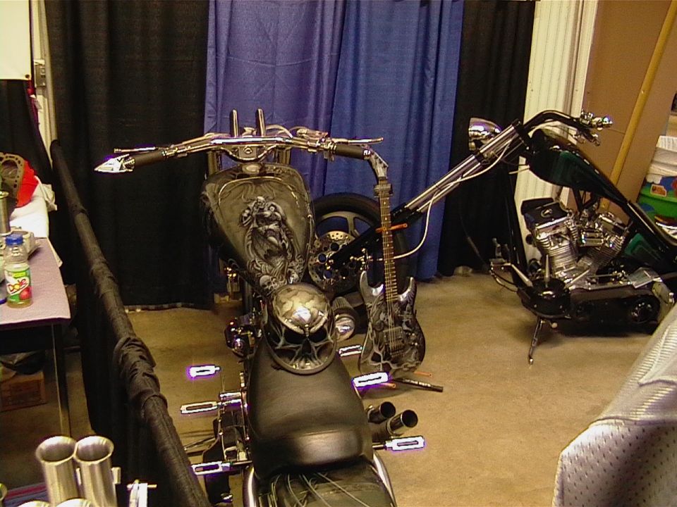 Front view of a custom motorcycle with skull helmet and electric guitar, another motorcycle in background