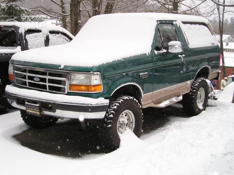 1996 Ford Bronco - A green 1996 Ford Bronco sits partially covered in snow, showing its lifted stance and large off-road tires.