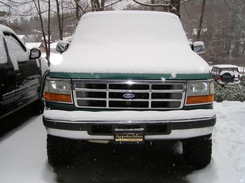 1996 Ford Bronco - A green 1996 Ford Bronco is parked outside and covered in snow, with another vehicle visible to the left and a smaller SUV in the backgroun…