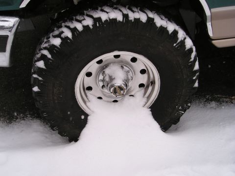 1996 Ford Bronco - A vehicle's tire is seen stuck in a pile of snow, highlighting its off-road tread.