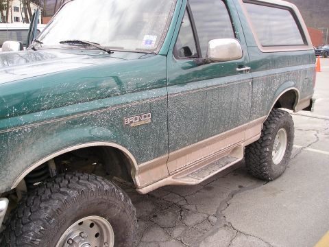 1996 Ford Bronco - A green 1996 Ford Bronco with tan trim and large off-road tires is shown from the side.