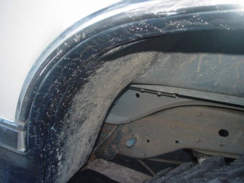 1986 Ford Bronco - Close-up inside a front wheel well of a white truck body with a dark blue fender flare and bright chrome/stainless wheel-opening trim. The…