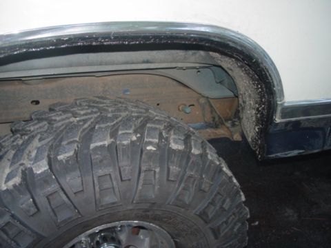 1986 Ford Bronco - Close-up of the rear wheel well of a lifted white truck with a chrome fender trim and black wheel-arch flare, showing bare inner fender she…