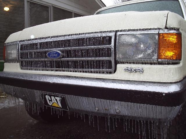 Ice-coated front grille of a white Ford 4x4 truck with icicles hanging from the bumper
