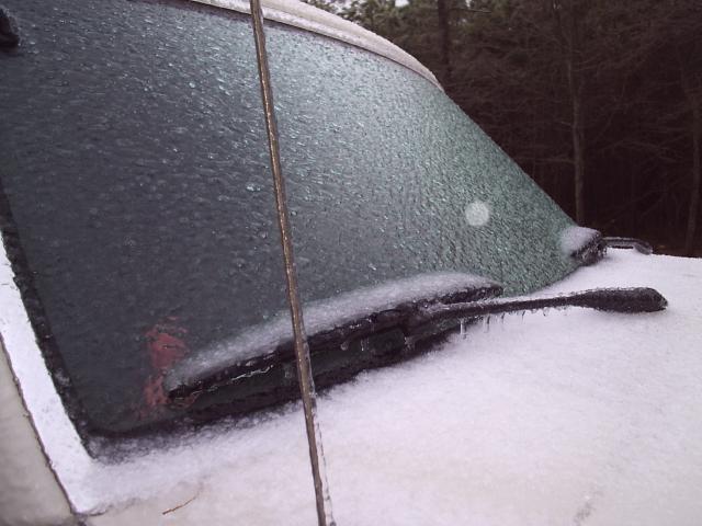 Windshield and wiper blades of a vehicle encased in ice, with snow on the hood