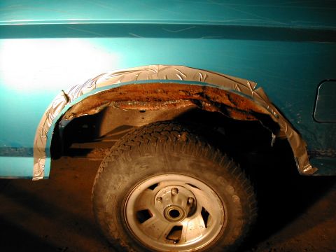 1994 Ford Bronco - Close-up of a vehicle's wheel well showing rust and makeshift fender trim.