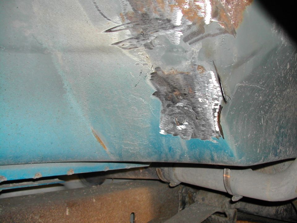 Close-up of rusted and cut metal on a teal vehicle's undercarriage near a pipe