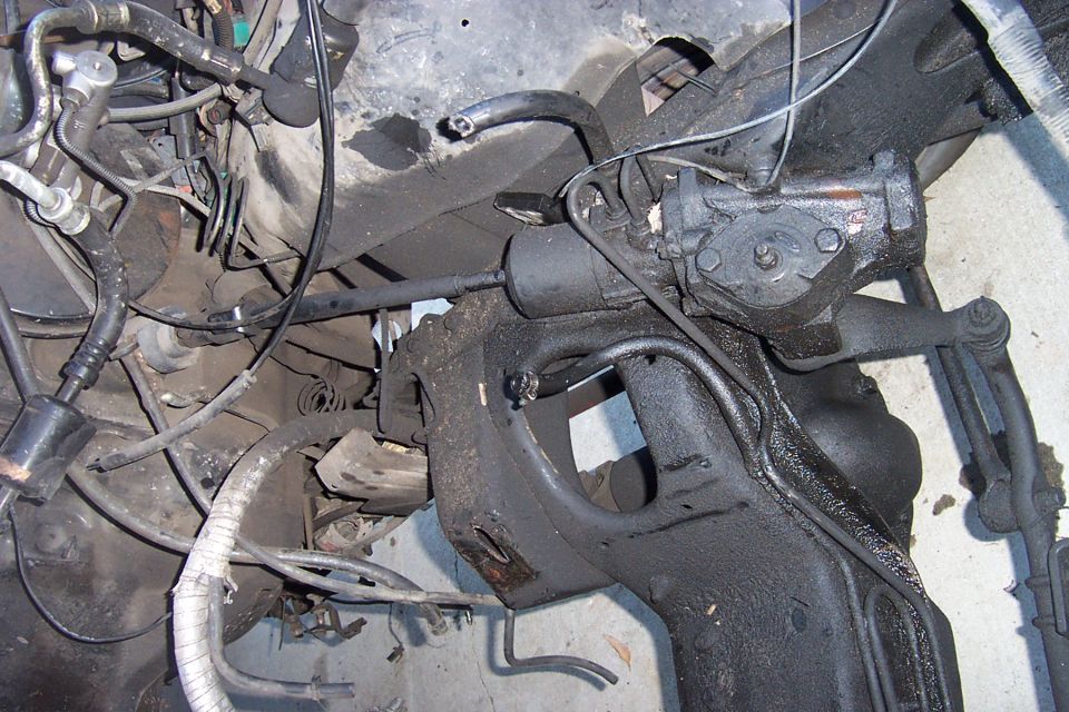 Underside view of front crossmember and steering gearbox with pitman arm, hoses and wiring