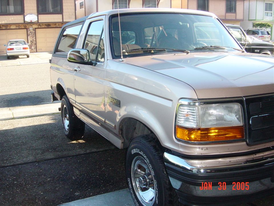 Tan 1992 Ford Bronco SUV parked on asphalt, front right quarter view. Chrome wheels and trim visible