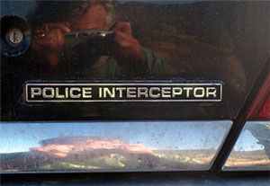 2000 Ford Crown Victoria - Close-up of the rear of a vehicle showing a 'POLICE INTERCEPTOR' badge and a Supermotors watermark.