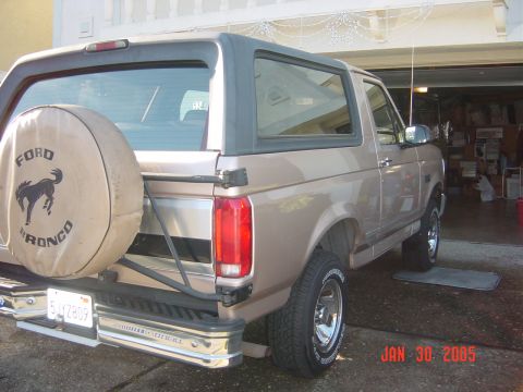 1990 Ford Bronco - A tan 1990 Ford Bronco is parked in a garage, showing its rear end and spare tire.