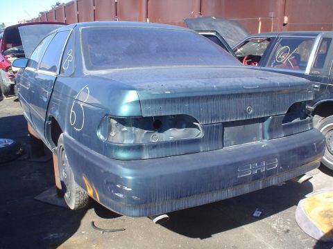 1993 Ford Taurus - Rear view of a dark teal 1993 Ford Taurus sedan in a junkyard, showing missing taillights and body damage.